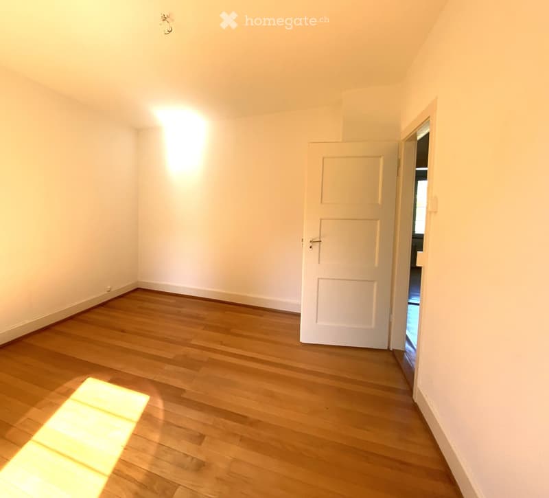 Empty room with wooden flooring and white walls, featuring a door leading to another space.