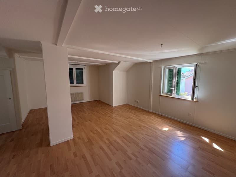 Empty room with wooden flooring, white walls, and two windows allowing natural light to enter.