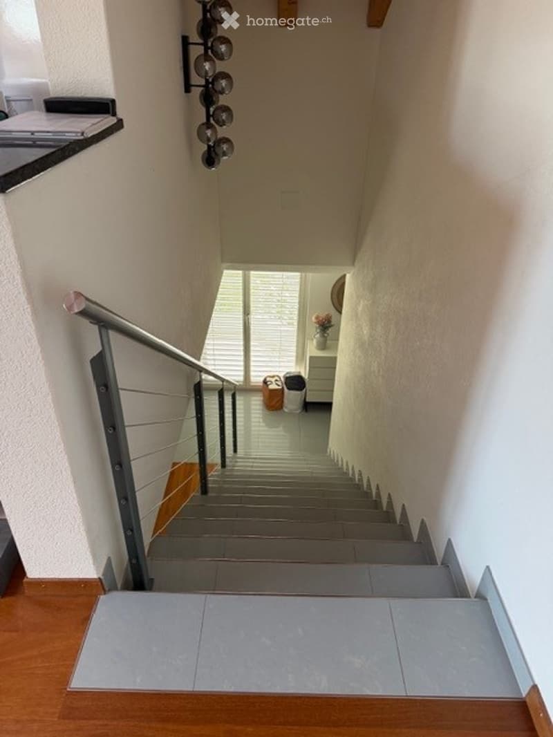 Modern staircase with metal railing and wooden steps, leading to an open area with a small table and vase.