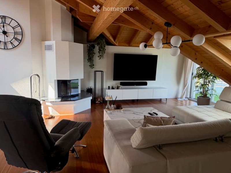 Modern living room with exposed wooden beams, a fireplace, a large flat-screen TV, a sectional sofa, a coffee table, and a comfortable armchair.