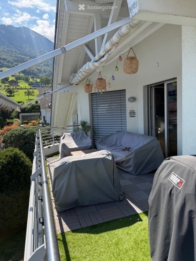 Balcony with covered seating area, covered furniture, hanging baskets, and scenic mountain view.