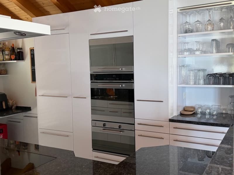 Modern kitchen with white cabinets, stainless steel oven, granite countertops, and glassware on display.
