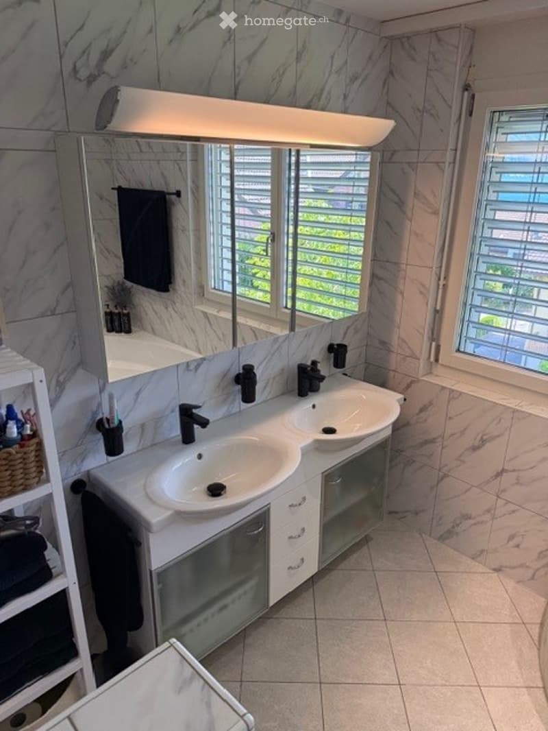 Modern bathroom with double sink vanity, marble tiles, large mirror, and natural light from windows.