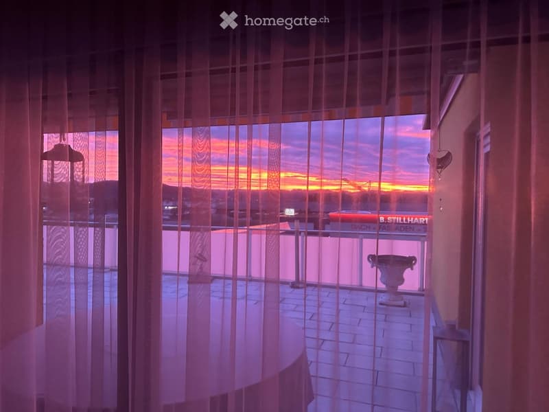 Balcony with terrace, table, railings, sunset view, vase, street name 'B. STILLHART'
