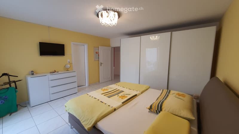 yellow walls, white tile floor, two twin beds, yellow pillows, wardrobe with sliding doors, dresser, TV mounted on wall, clothes rack