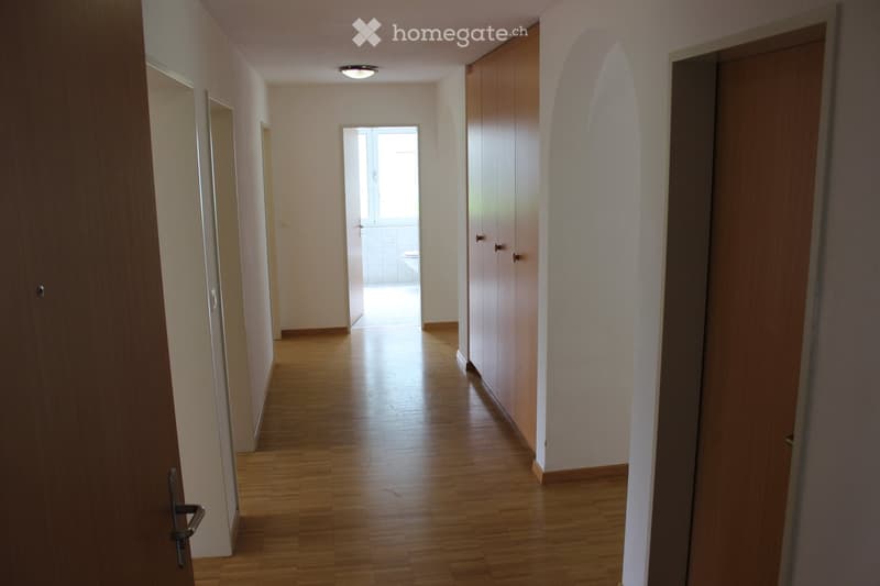 Empty hallway with wooden flooring, white walls, and a recessed ceiling light. Doors on both sides lead to other rooms.