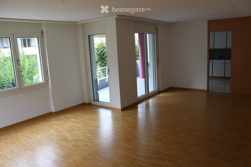 Empty room with wooden flooring, large windows, and sliding glass doors leading to a balcony.
