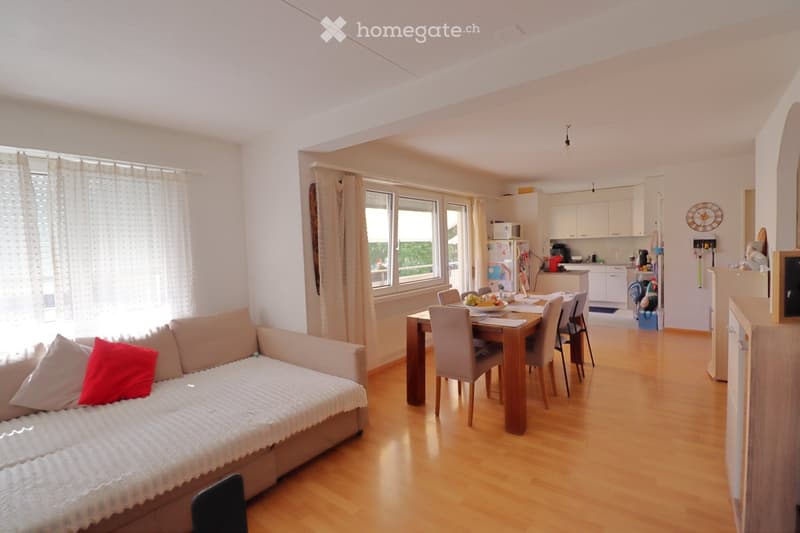 A modern, open-concept living and dining area with a sofa, dining table, chairs, and a small kitchen area with cabinets and appliances.