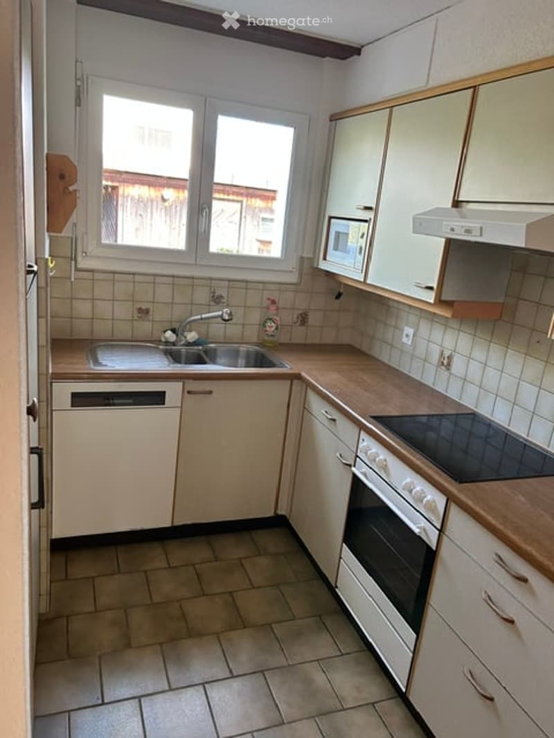 Compact kitchen with light-colored cabinets, a sink, microwave, oven, and dishwasher. The space features tiled walls and a wooden countertop.