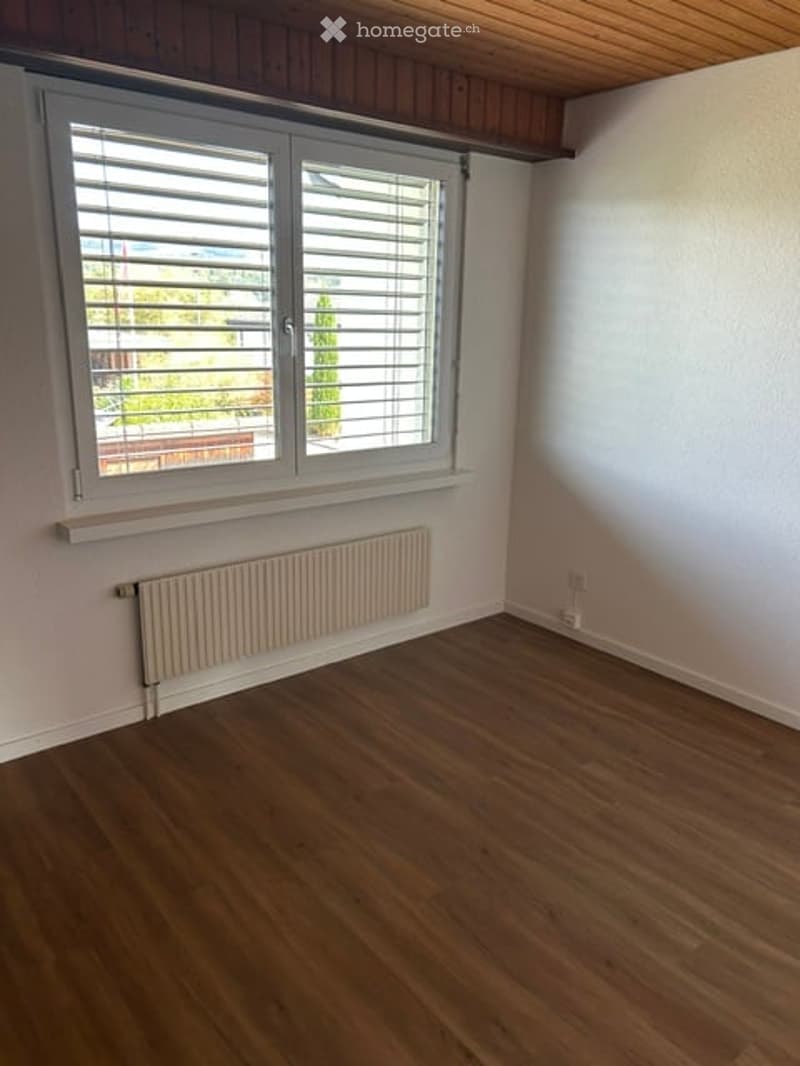 Empty room with wooden flooring, white walls, a window with blinds, and a radiator below the window.