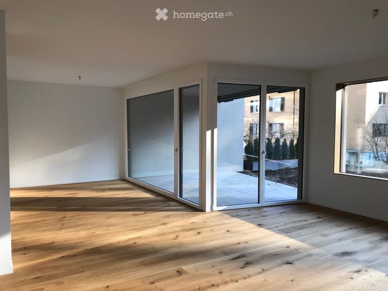 Empty room with wooden flooring, large sliding glass doors, and natural light streaming in.