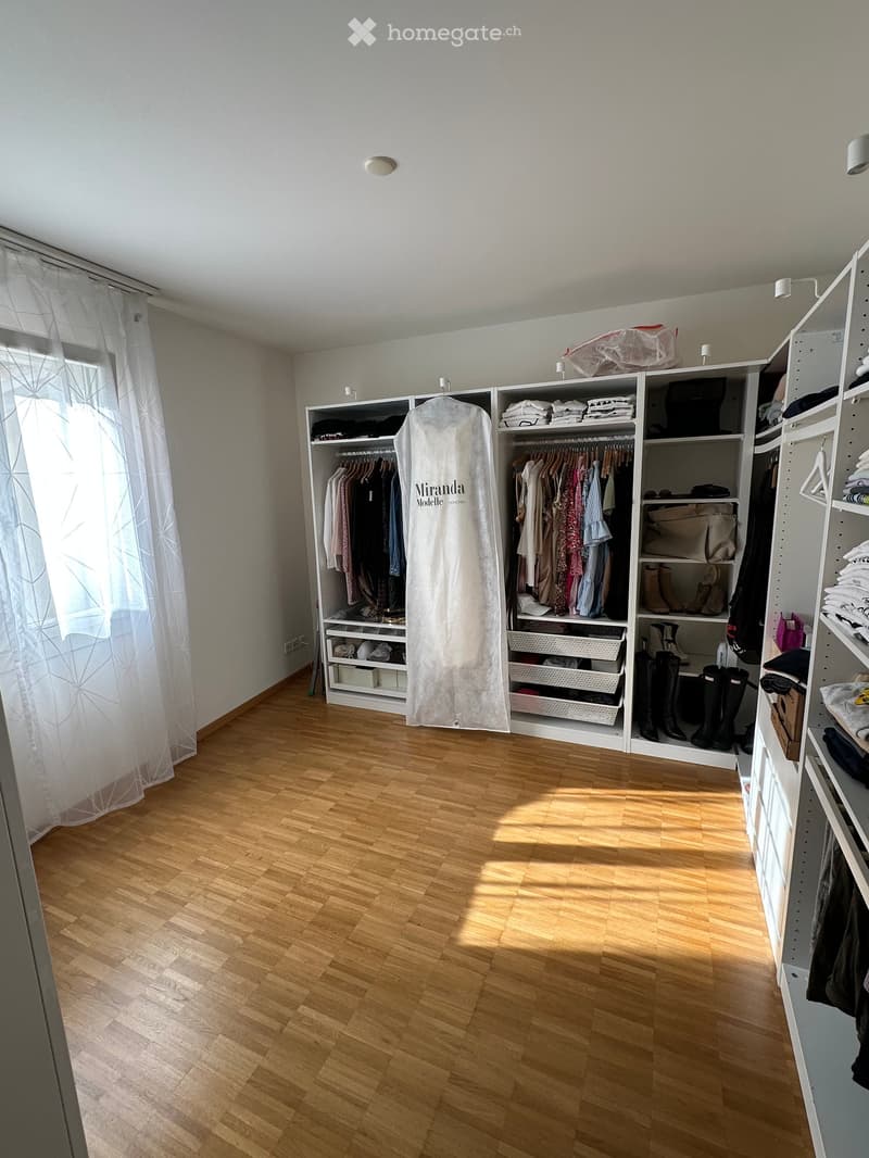Empty room with wooden flooring, large built-in wardrobe with multiple sections, and a window with white curtains.