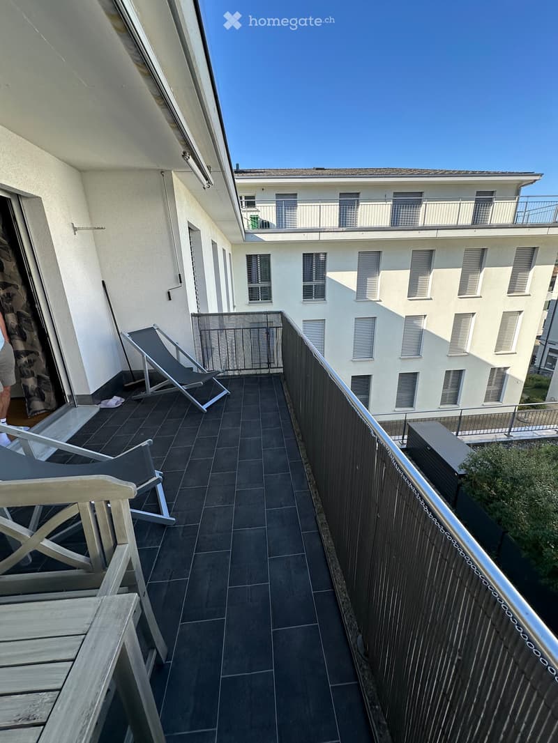 Balcony with dark tiled floor, metal railing, and two lounge chairs.