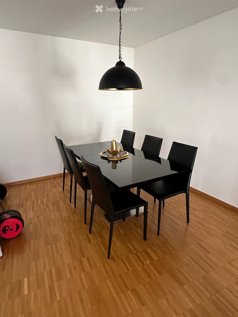Dining room with a black glass table, six black chairs, and a hanging pendant light. A decorative candle is placed on the table.