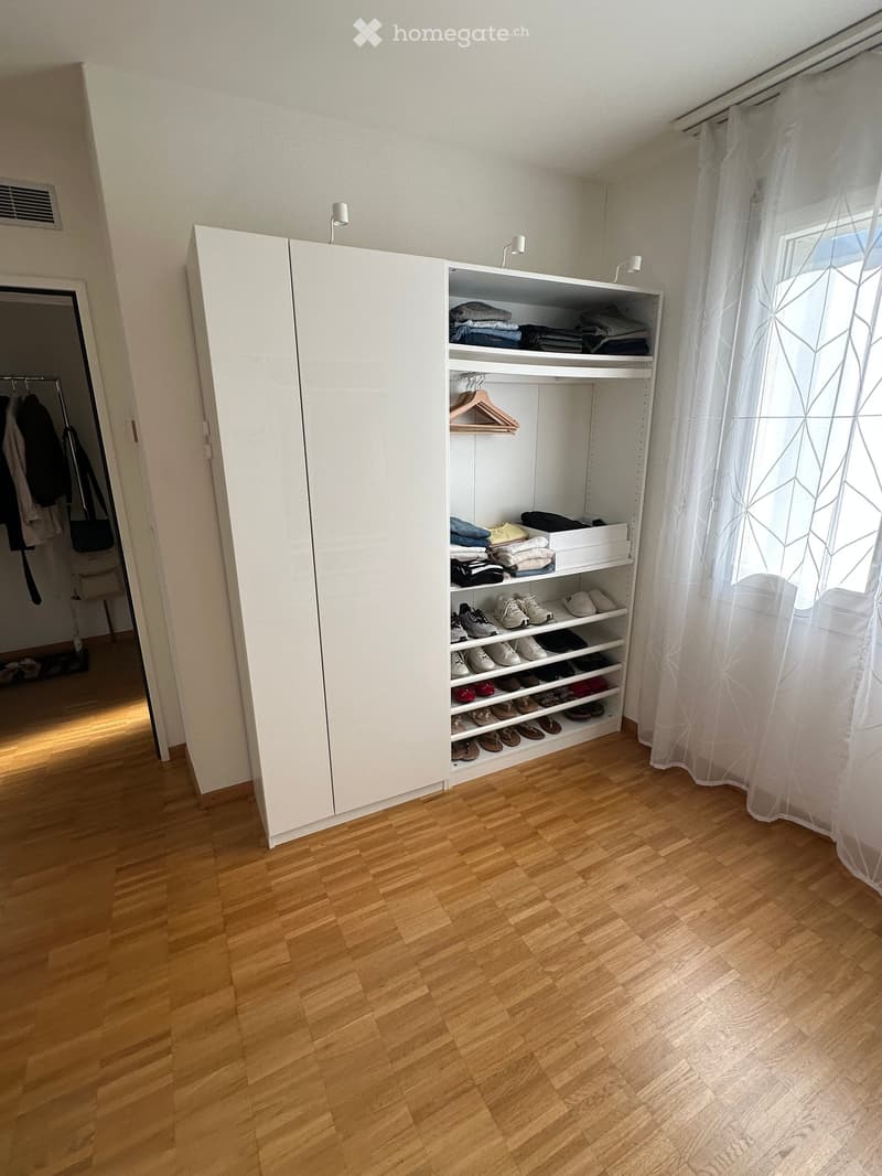 Empty room with wooden flooring, white built-in closet, and white curtain on the window. No furniture or personal items visible.