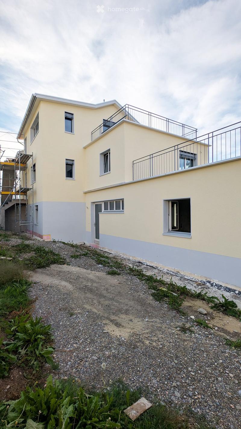 Two-story house with yellow and gray exterior, multiple windows, and a balcony on the upper level.
