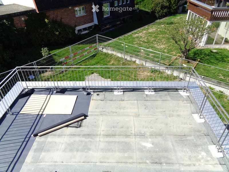 Roof terrace with metal railing, concrete surface, and a small grassy area in the background.
