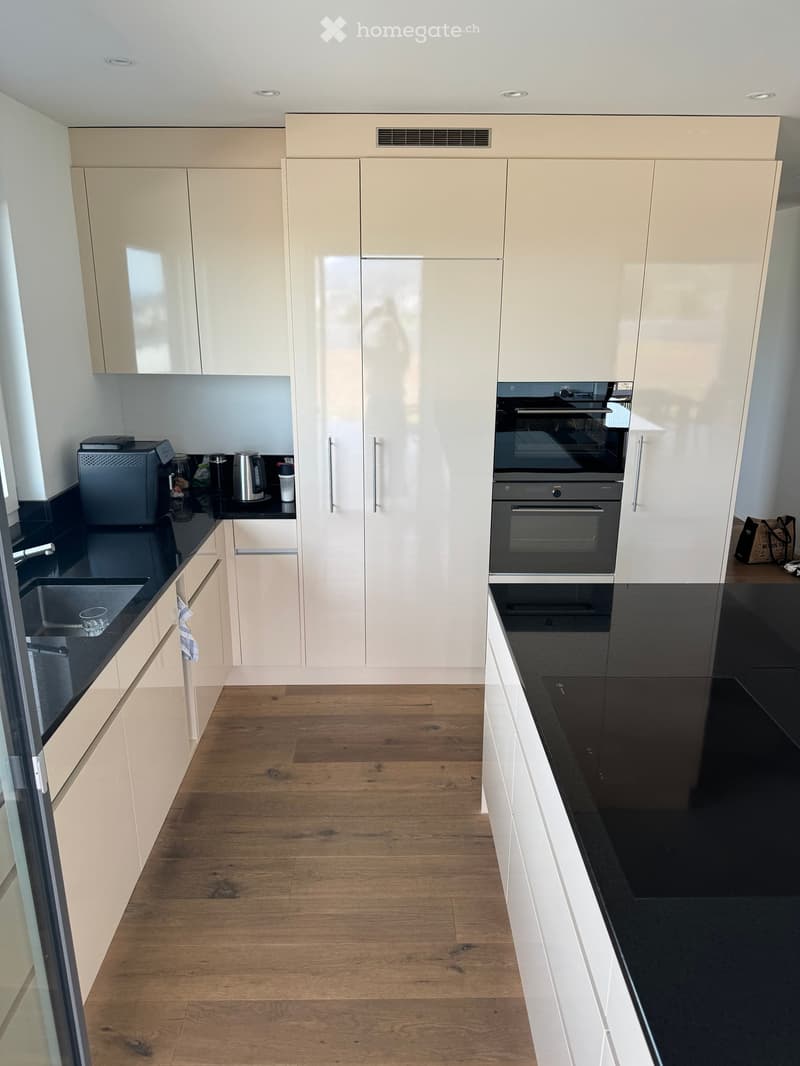 Modern kitchen with light-colored cabinets, black countertops, and wooden flooring. Features include a sink, oven, and various appliances.