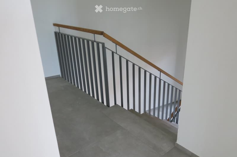 Corridor / Hallway. Modern staircase with grey tiled steps, white walls, and a wooden handrail with metal balustrade.