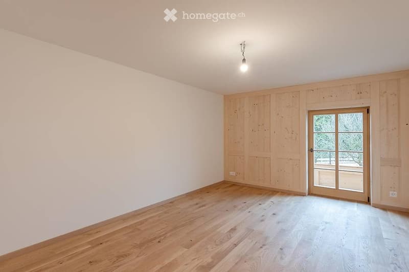 Empty room with wooden flooring, white walls, and a large glass door leading to a balcony.