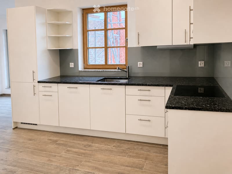Modern kitchen with white cabinets, granite countertops, and a window overlooking a tiled roof.