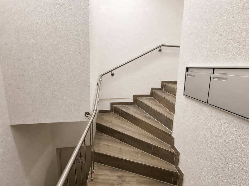 Modern staircase with wooden steps and a metal handrail, leading up to a landing area with built-in storage units.