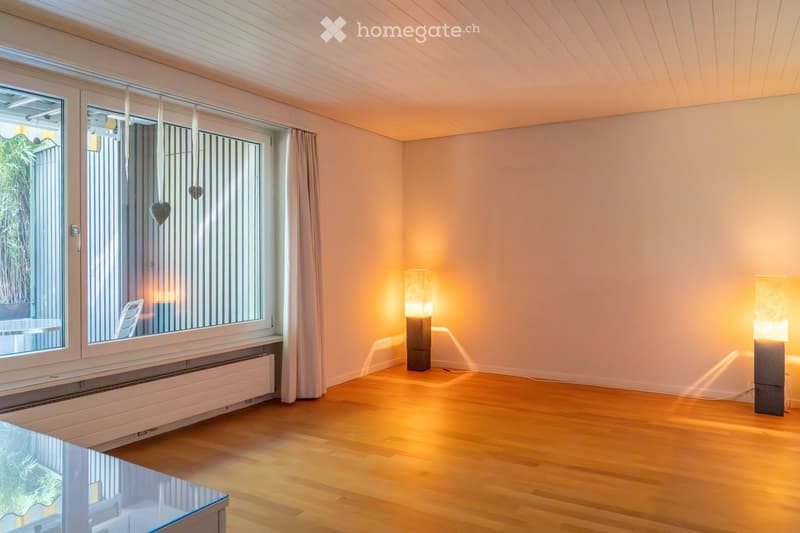 Empty room with wooden flooring, large windows with curtains, two table lamps, and a radiator under the windows.
