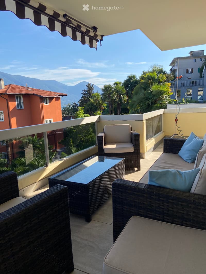 Balcony with wicker furniture, including a sofa, chairs, and a coffee table, overlooking a scenic mountain view.