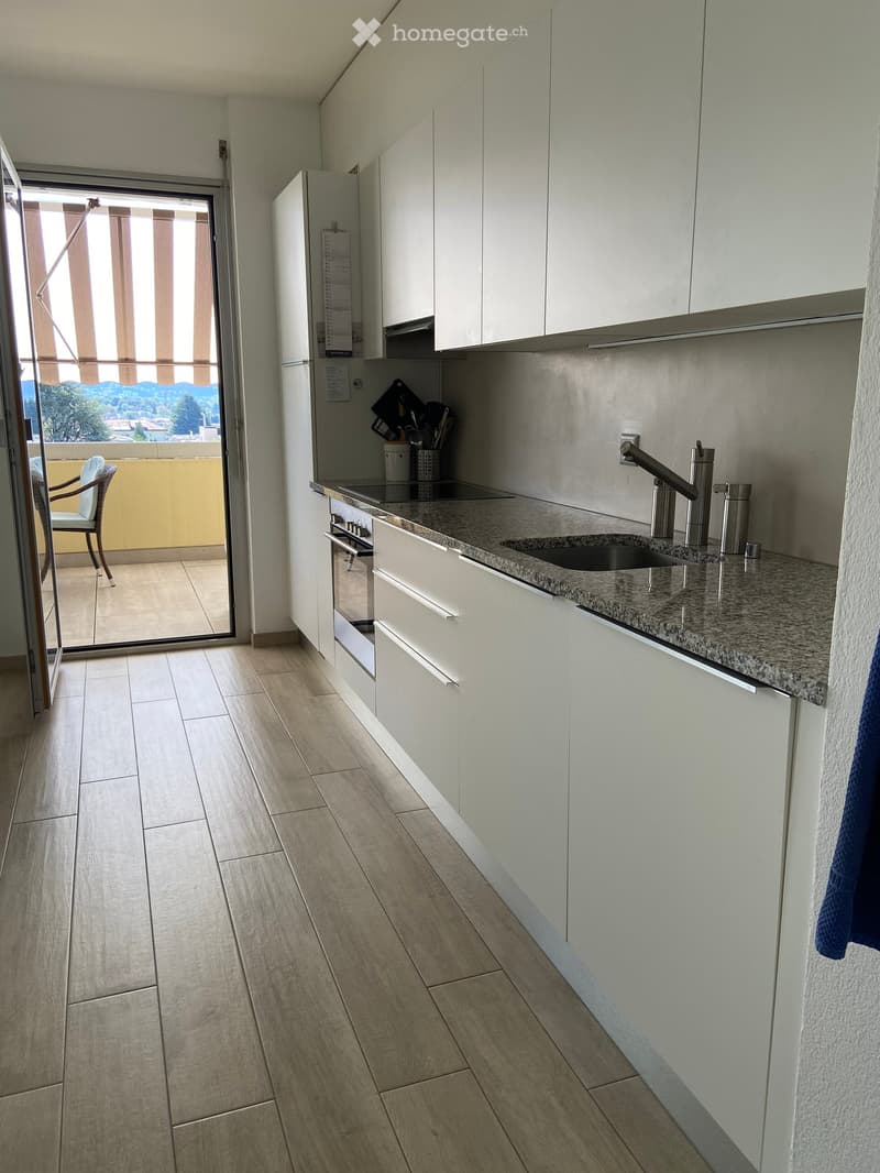 Modern kitchen with white cabinets, granite countertop, stainless steel sink and faucet, and a view of the balcony.