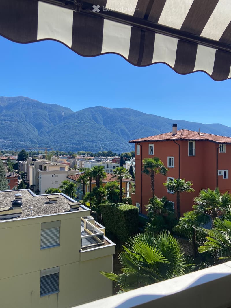 Balcony with a scenic view of mountains and a town, surrounded by palm trees and buildings.