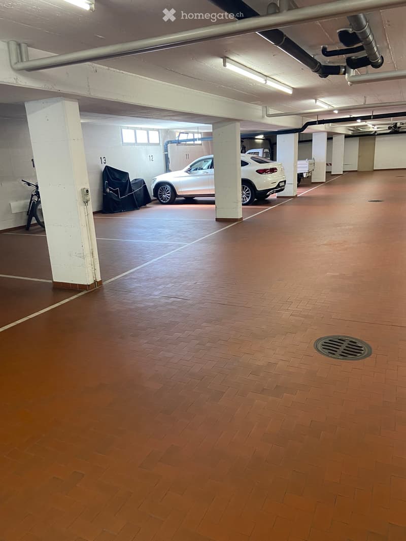 Underground parking area with wooden flooring, white pillars, and a parked car and bicycle.