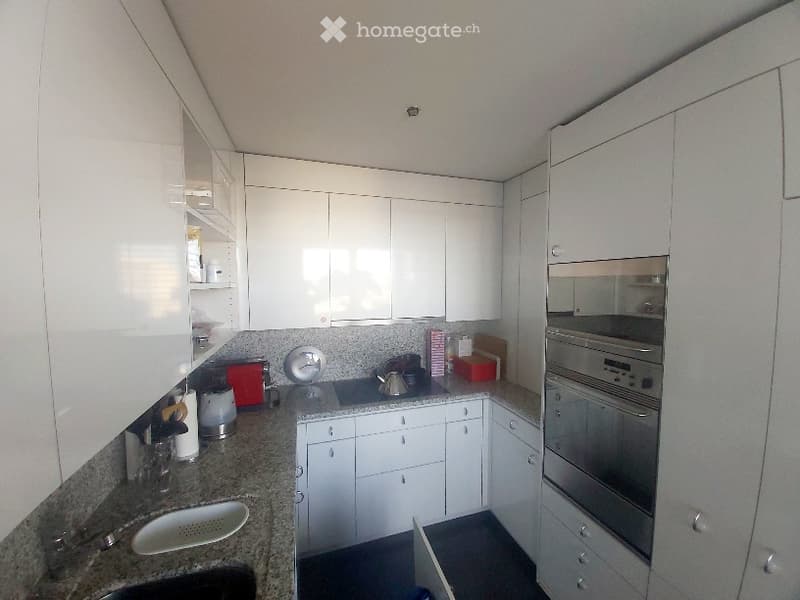 Modern kitchen with white cabinets, stainless steel oven, granite countertop, and various small appliances.