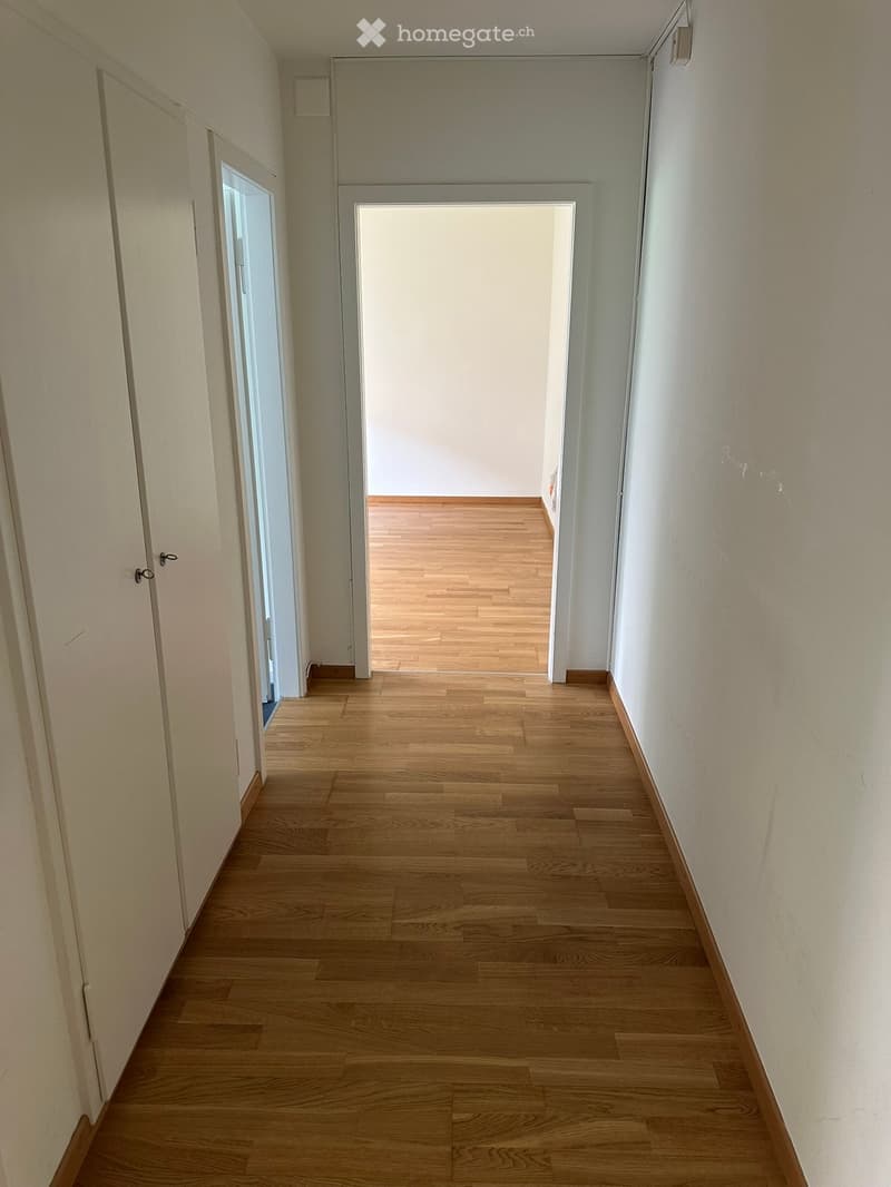 Empty hallway with wooden flooring, white walls, and two doors on either side, one leading to another room.