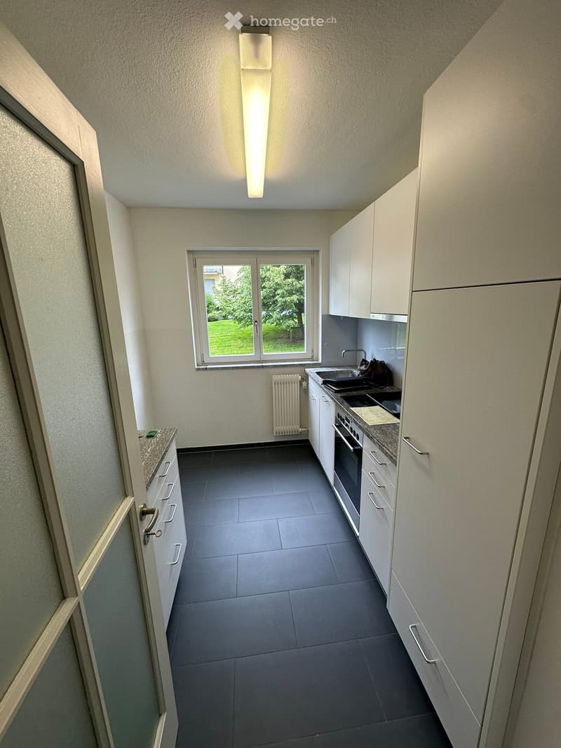 Modern kitchen with white cabinets, dark tiled floor, sink, oven, and radiator.