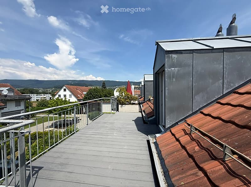 Wooden balcony with metal railing, overlooking a residential area with houses and greenery.