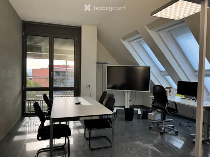 Bright, modern office space with large windows, a long white table surrounded by black chairs, and two large screens mounted on stands.