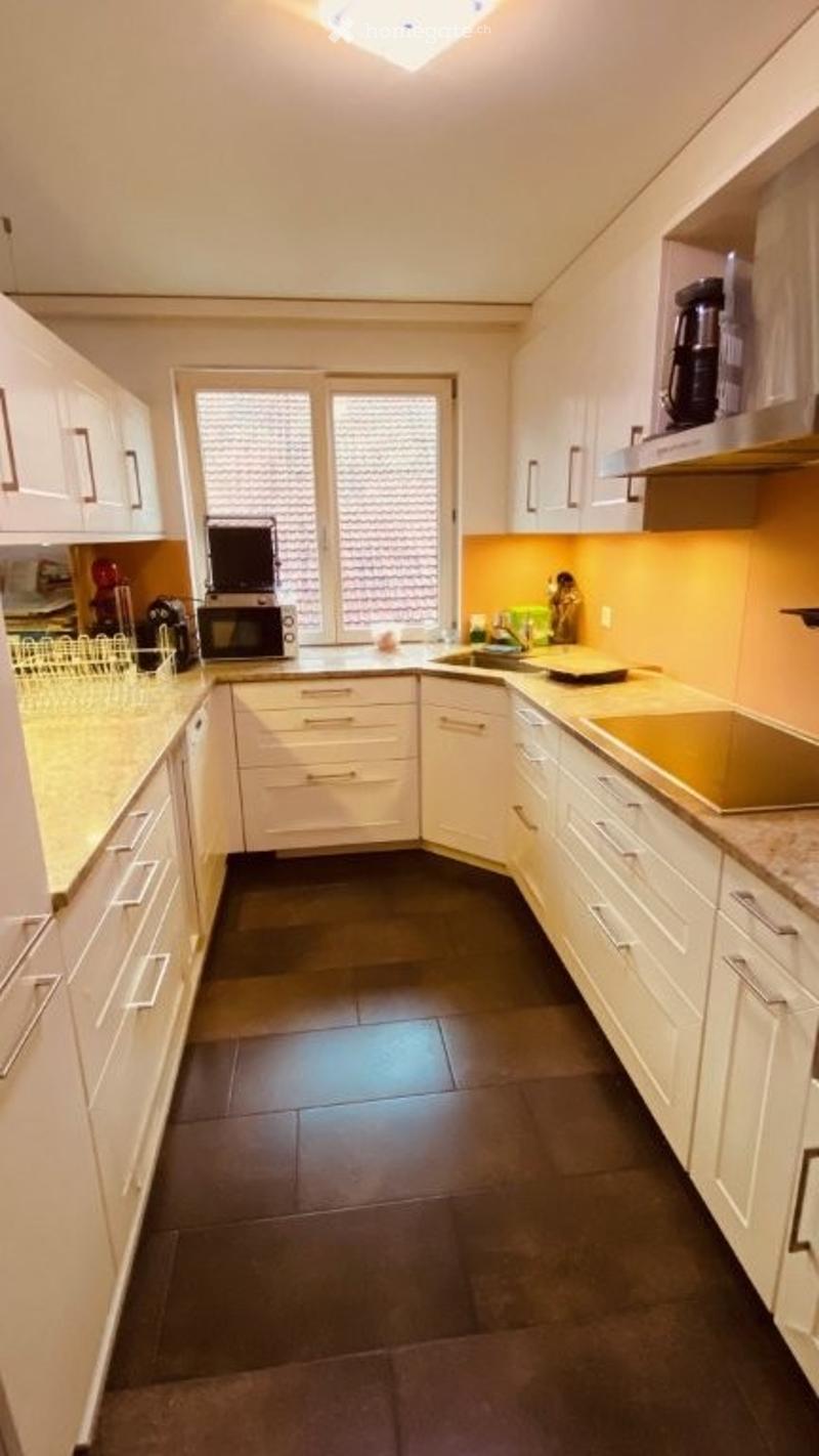 Modern kitchen with white cabinets, dark tiled floor, and stainless steel appliances. Features a microwave, coffee maker, and a sink.