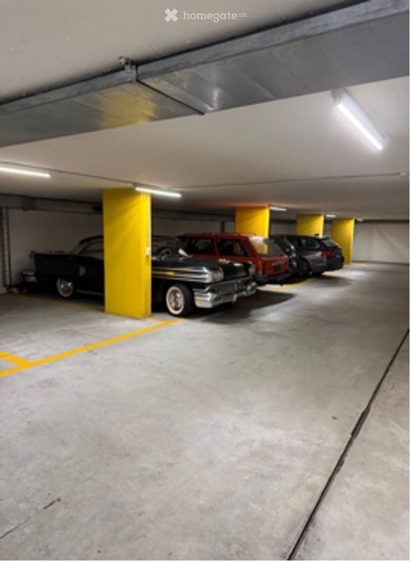 Underground parking area with several cars parked, yellow pillars, and concrete floors.
