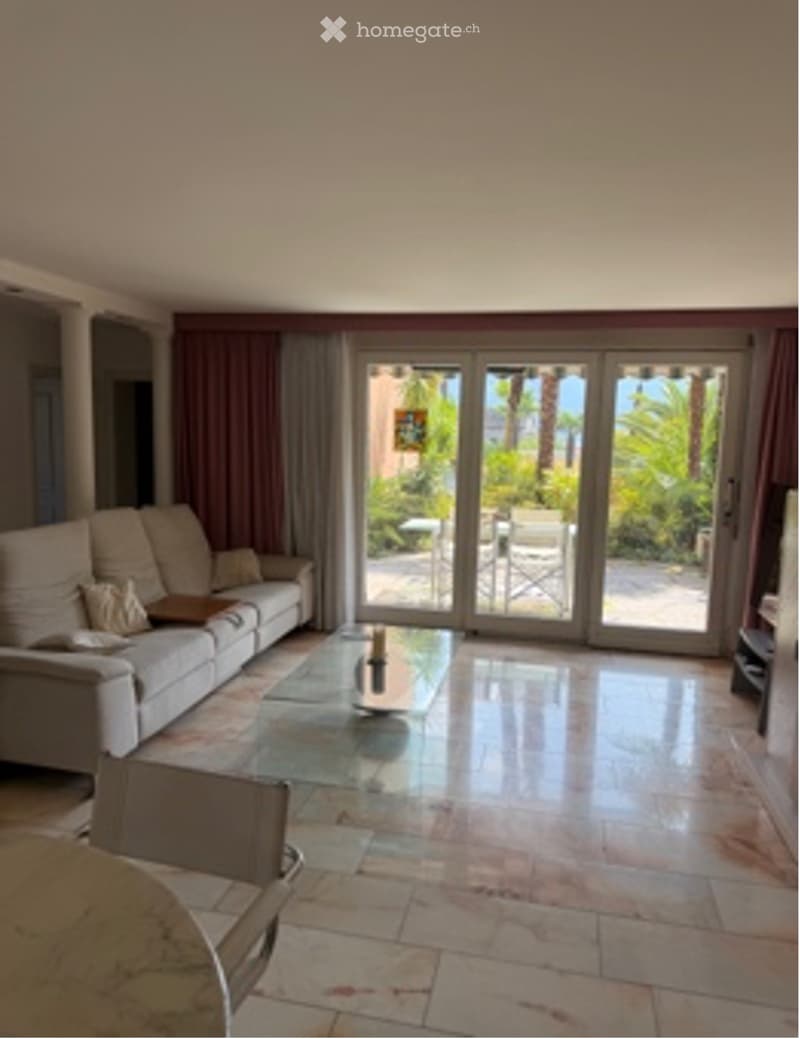 Spacious living room with a white sofa, glass coffee table, and large sliding glass doors leading to an outdoor area.