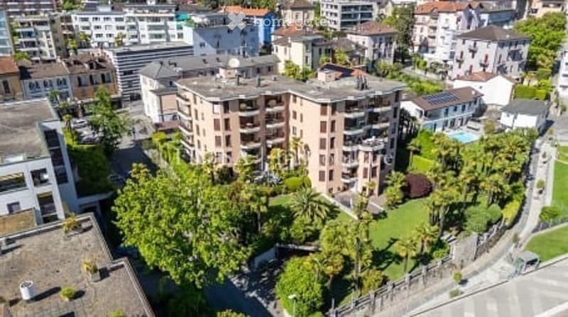 Aerial view of a multi-story residential building surrounded by greenery and a swimming pool.