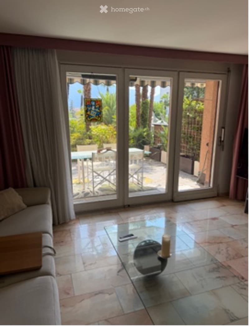 Living room with tiled floor, large sliding glass doors leading to a patio, sofa, coffee table, and candle on the table.