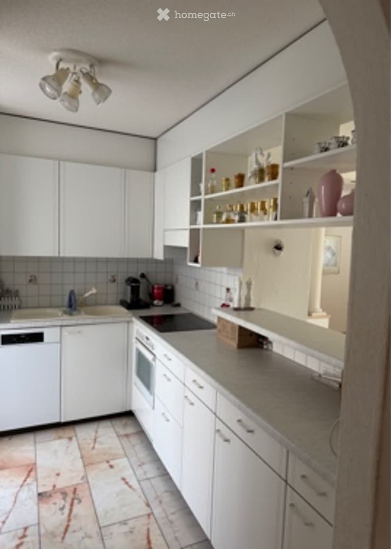 Modern kitchen with white cabinets, stainless steel appliances, and a grey countertop. Features include a sink, faucet, oven, dishwasher, coffee maker, and decorative vases on shelves.