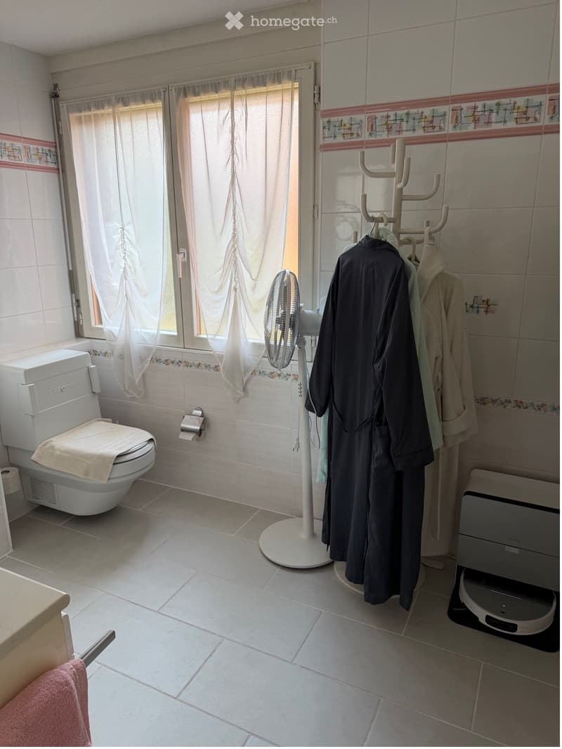 Bathroom with a toilet, fan, robe, towel, toilet paper, and a bathrobe rack.