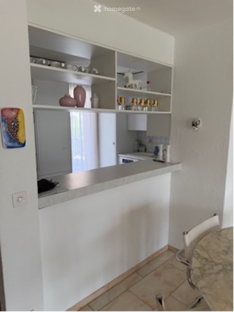 Modern kitchen with white cabinets, open shelving, and a small seating area with a chair.