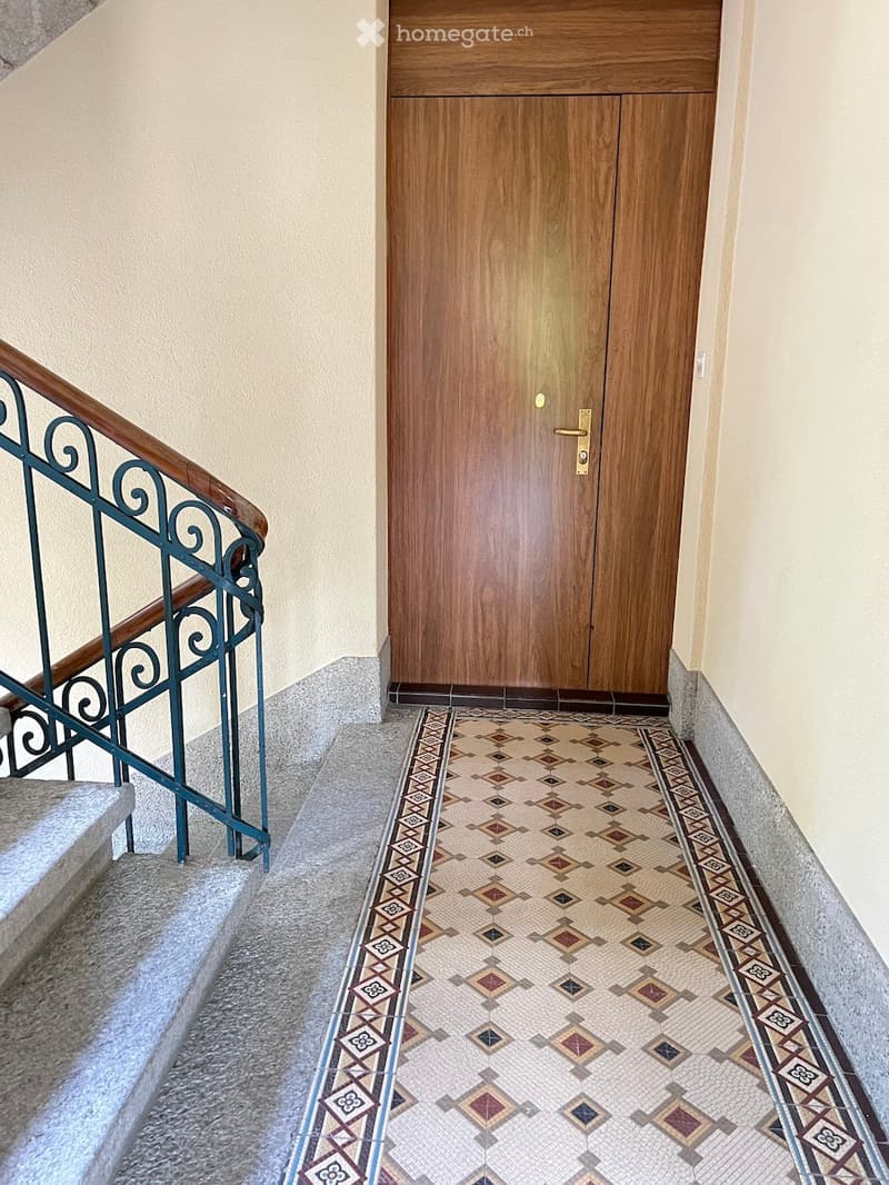 Staircase with decorative tile floor and wooden double doors at the end.