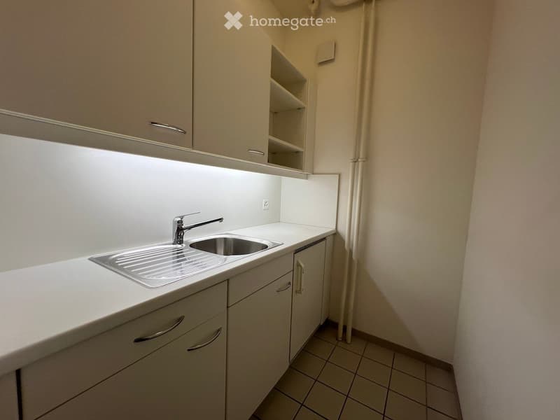 Compact kitchen with white cabinets, a stainless steel sink, and a faucet. The space includes built-in storage and a tiled floor.