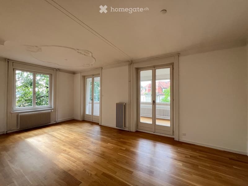 Empty room with wooden flooring, large windows, and sliding glass doors leading to a balcony.