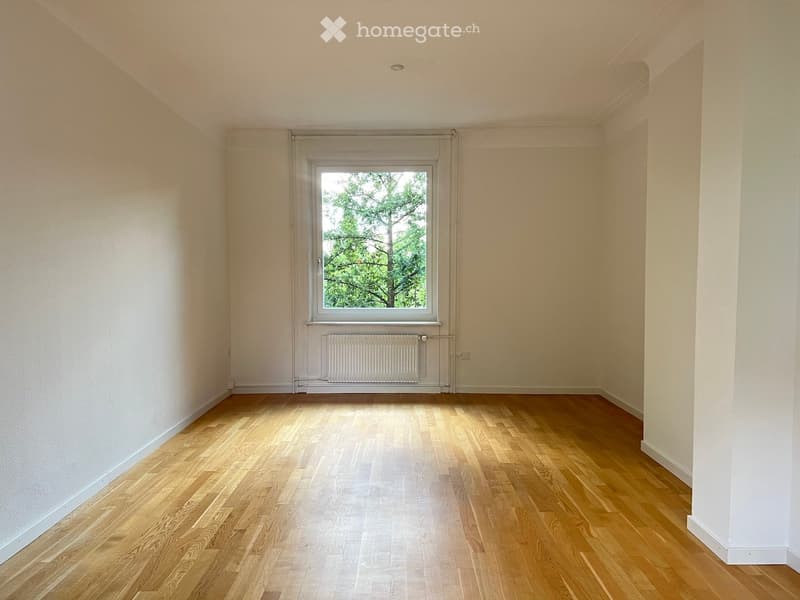 Empty room with wooden flooring, white walls, and a single window with a radiator below it.
