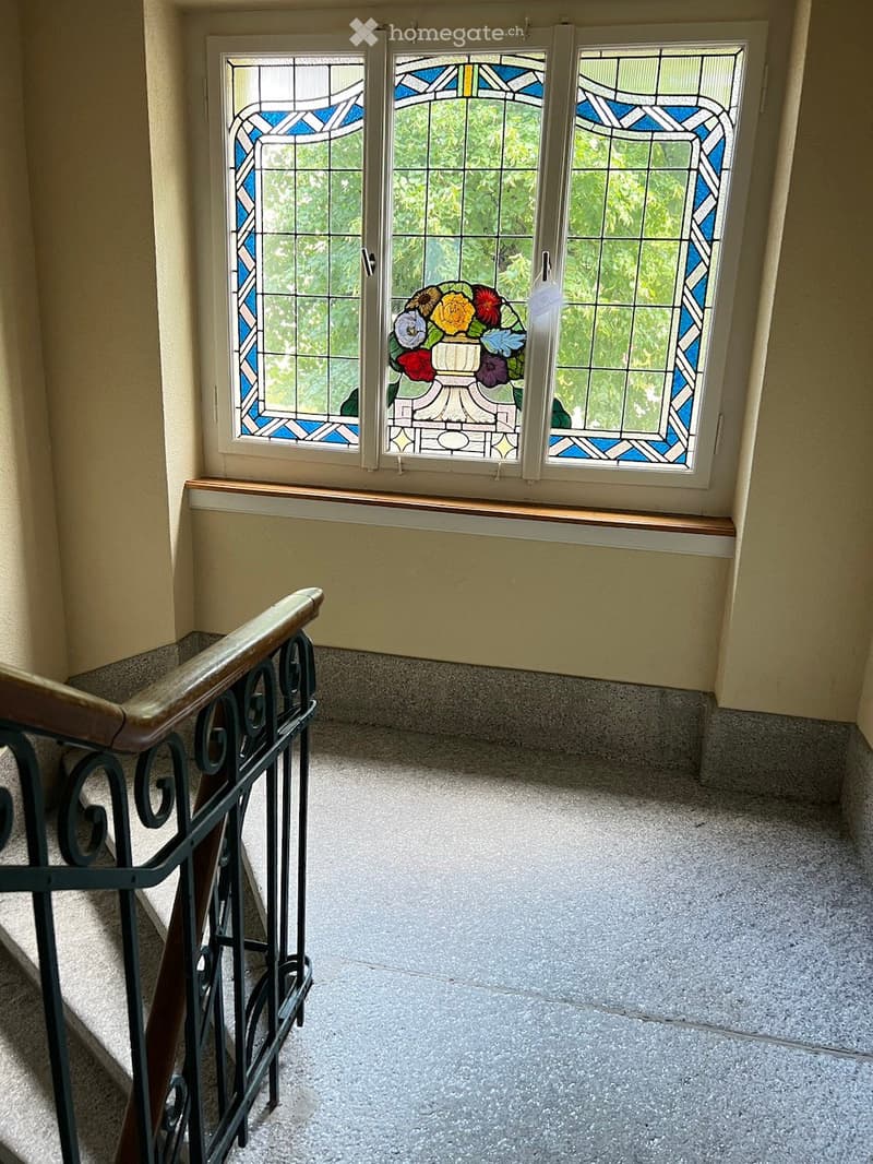 Hallway with stained glass windows, wooden railing, and carpeted stairs.