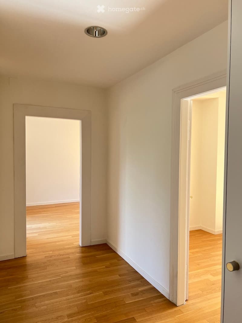 Empty room with light-colored walls and wooden flooring, featuring two open doorways leading to adjacent spaces.